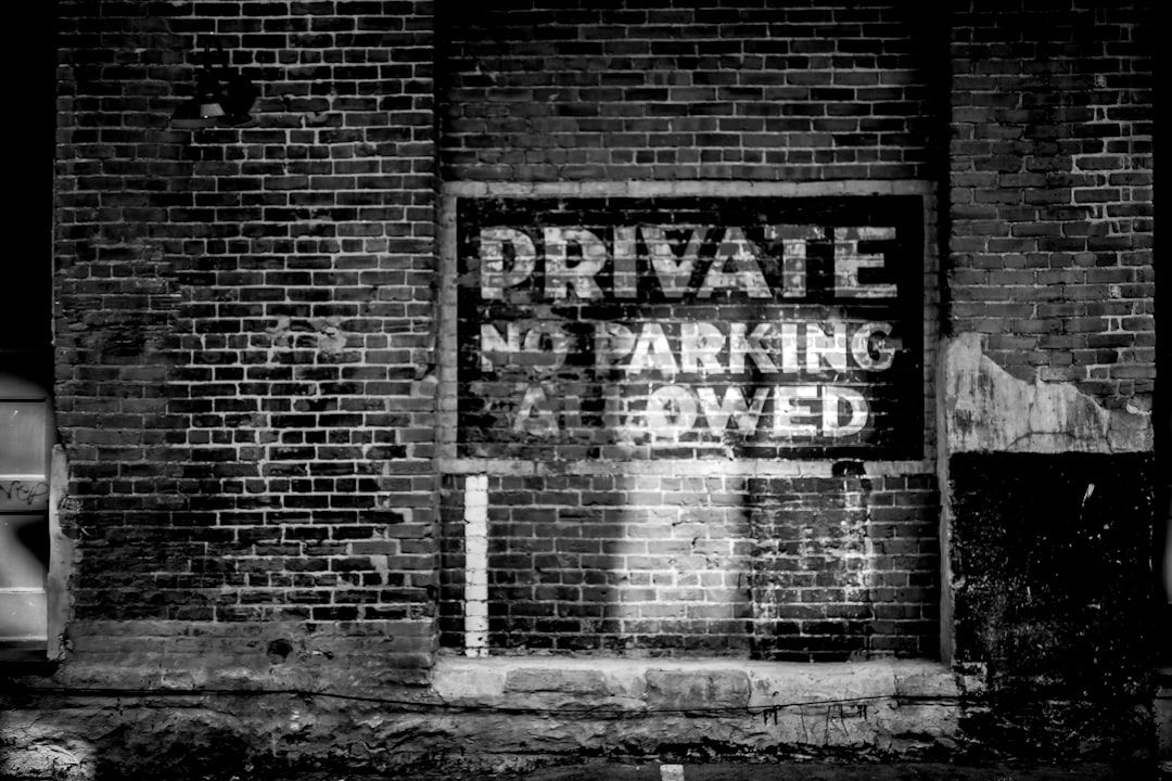 Svartvit bild av tegelvägg med 'PRIVATE NO PARKING ALLOWED' målat