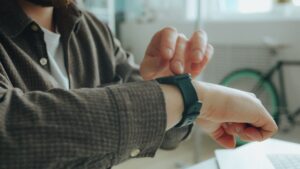 Person justerar en smartklocka med svart armband vid ett skrivbord