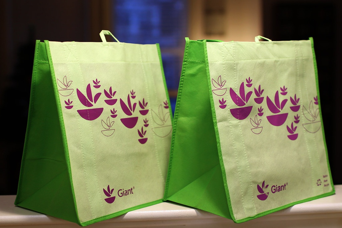 Två gröna återanvändbara shoppingkassar från Giant supermarket med lila blommönster. Kassarna har starka handtag och en strukturerad form som gör att de står upprätt.