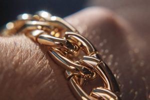 Närbild av ett glänsande guld Bismarckarmband på handleden, med hud och hår synligt.