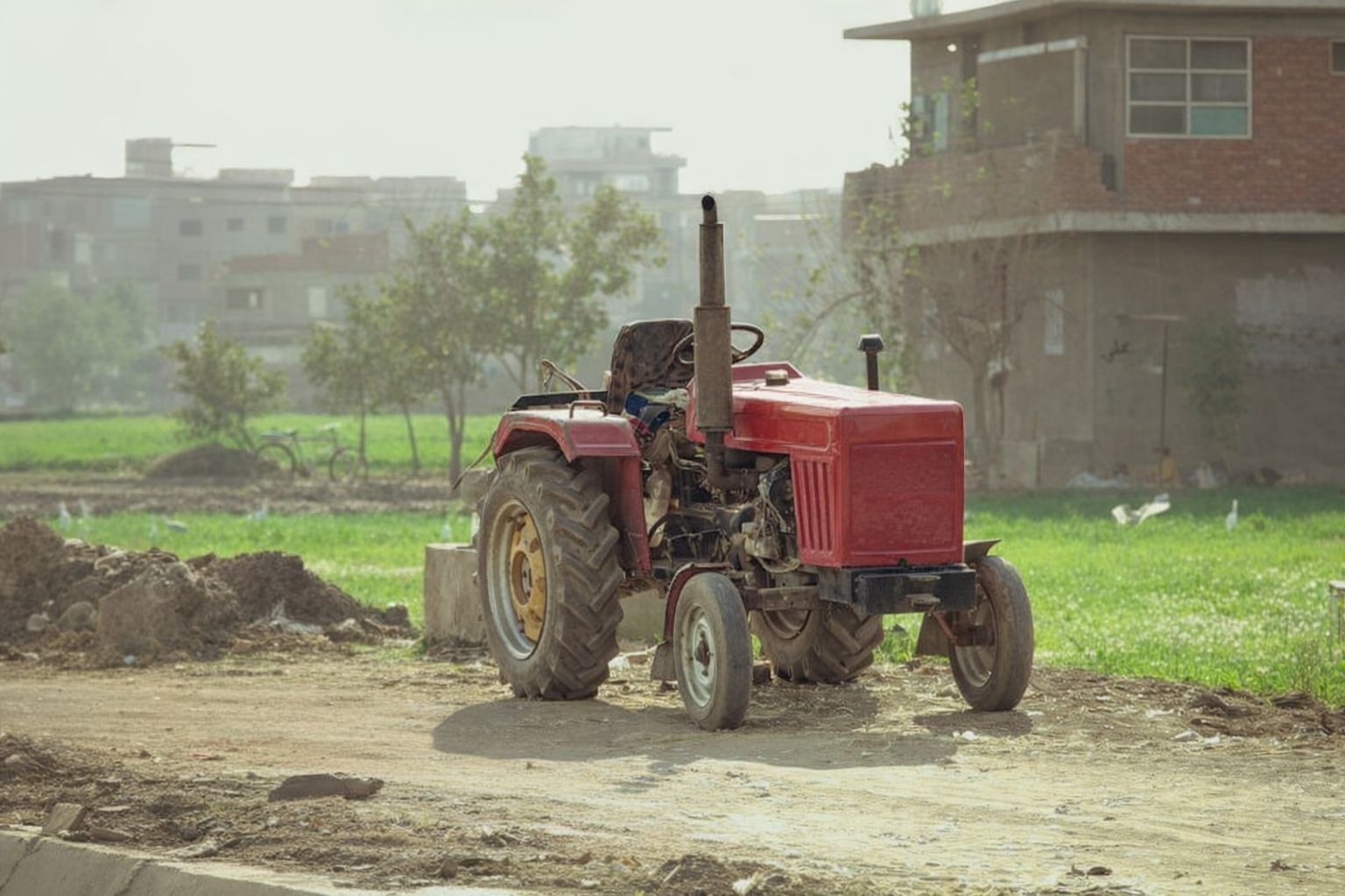 En röd, äldre traktor står parkerad på en grusväg i ett lantligt område.